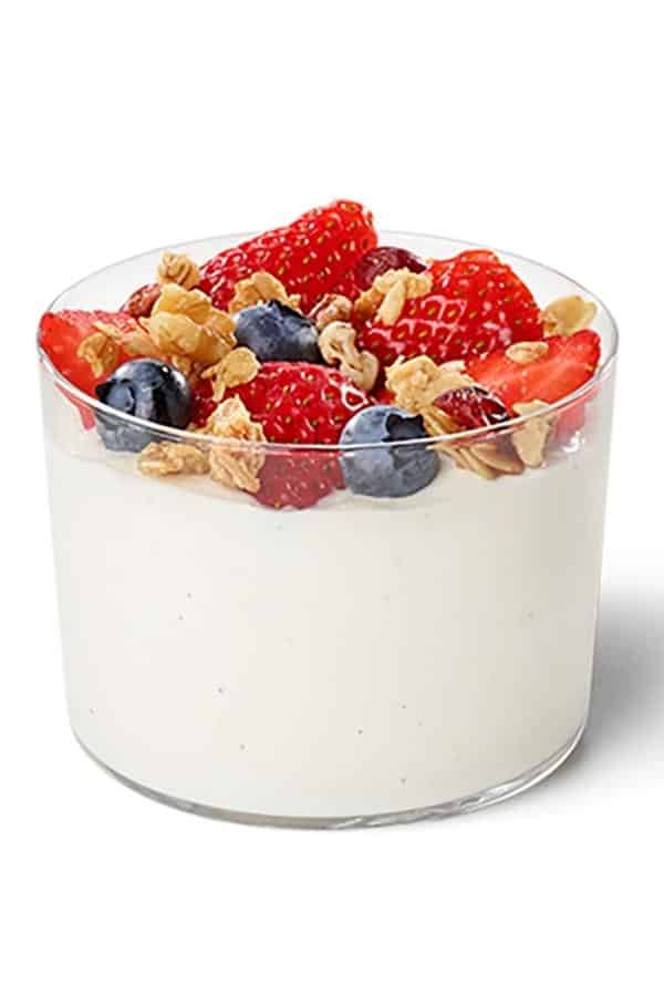 Strawberris, granola, and blueberries on top of yogurt in a glass cup.