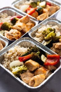 A coupled of individual containers filled with chicken, rice, and veggies.