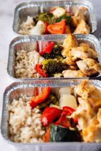 Three individual containers with rice, veggies, and chicken in it.