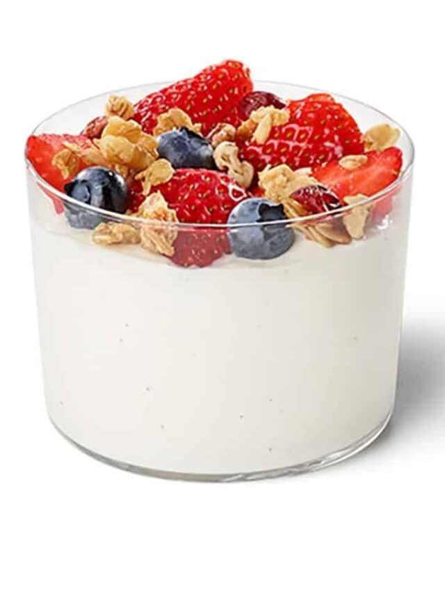 Strawberris, granola, and blueberries on top of yogurt in a glass cup.