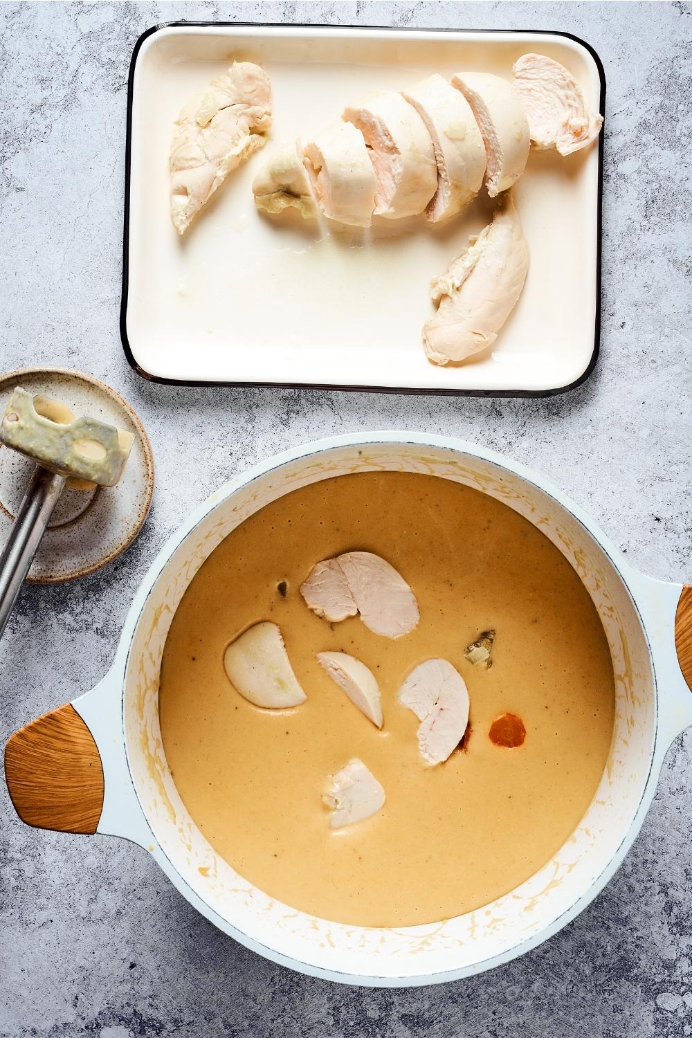 Buffalo chicken soup with chicken pieces in a white bowl. Behind it is a rectangular plate with chicken pieces on it.