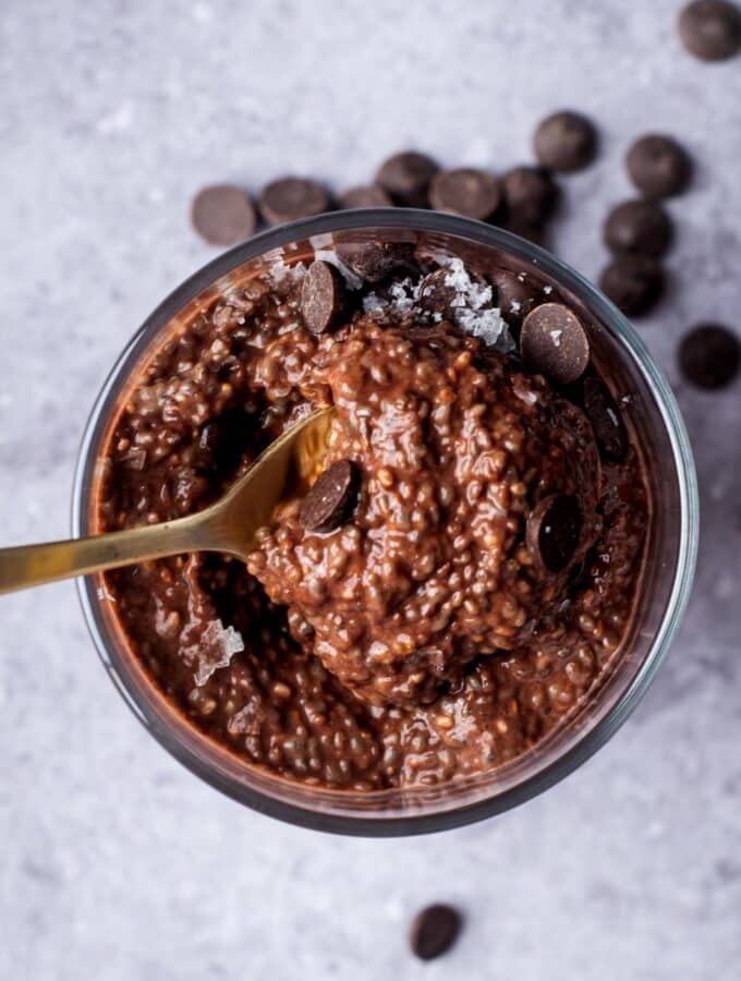 A spoon scooping chocolate protein pudding out of a glass that is filled with the pudding.