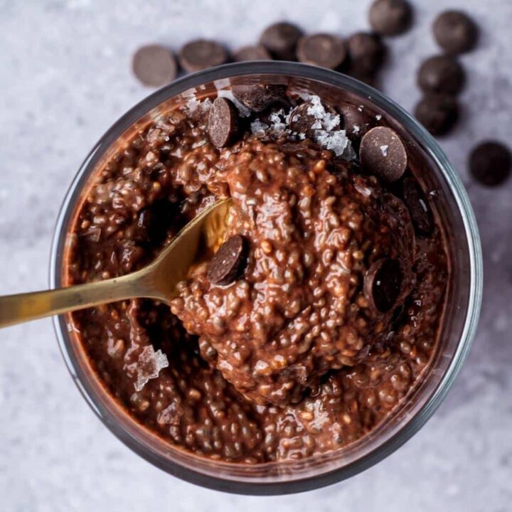 A spoon scooping chocolate protein pudding out of a glass that is filled with the pudding.