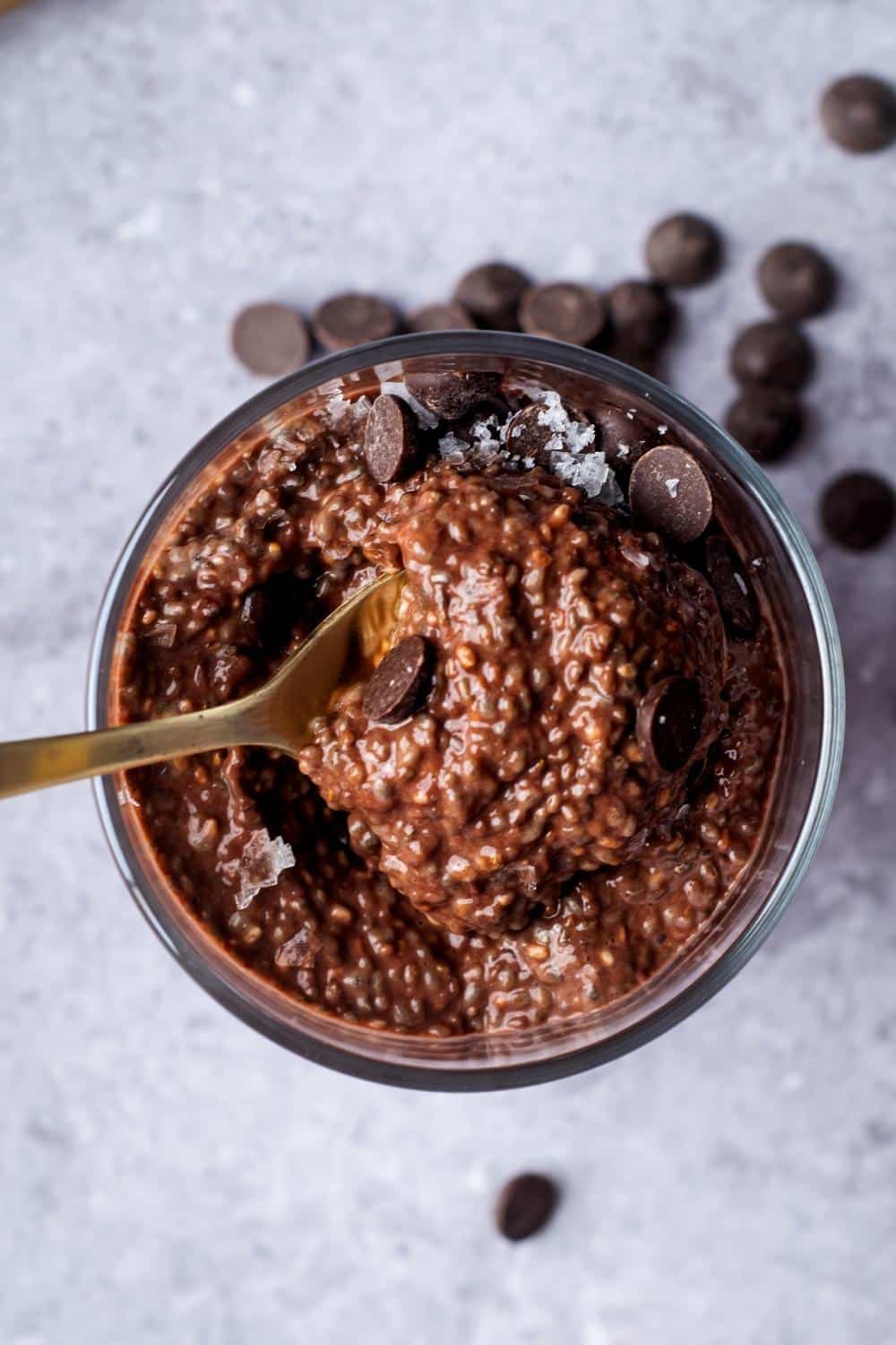 A spoon scooping chocolate protein pudding out of a glass that is filled with the pudding.