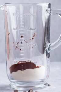 A glass blender with protein powder and almond milk in it.