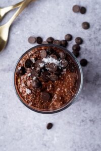 Chocolate chips and sea salt flakes on top of chocolate protein pudding in a cup.