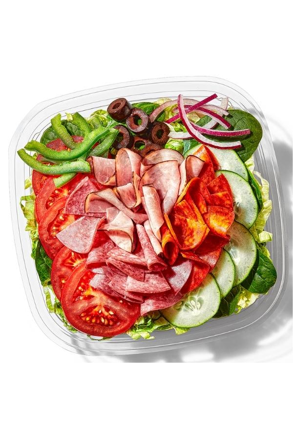 Salami, Ham, and pepperoni with tomato, olives, and onion on top of lettuce in a container.