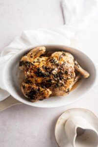 A cornish hen in a white casserole dish on a counter.