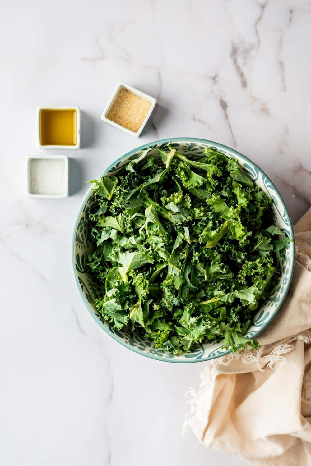 Kale chips in a bowl, oil in a bowl, salt in a bowl, and parmesan cheese in a bowl.