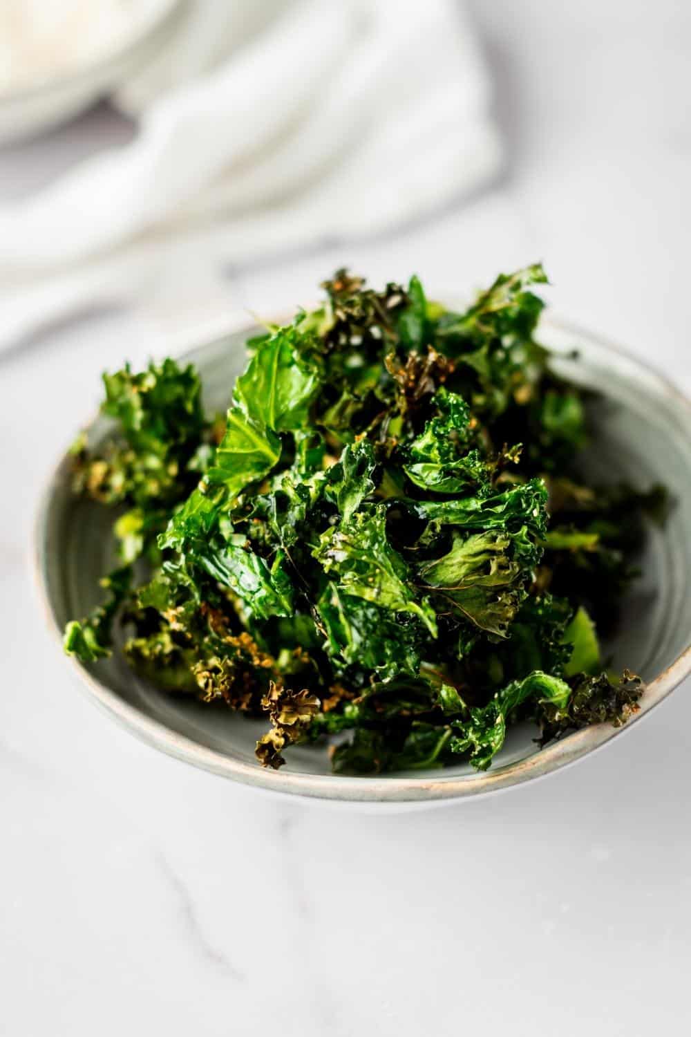 Kale chips in a white bowl on a white counter.