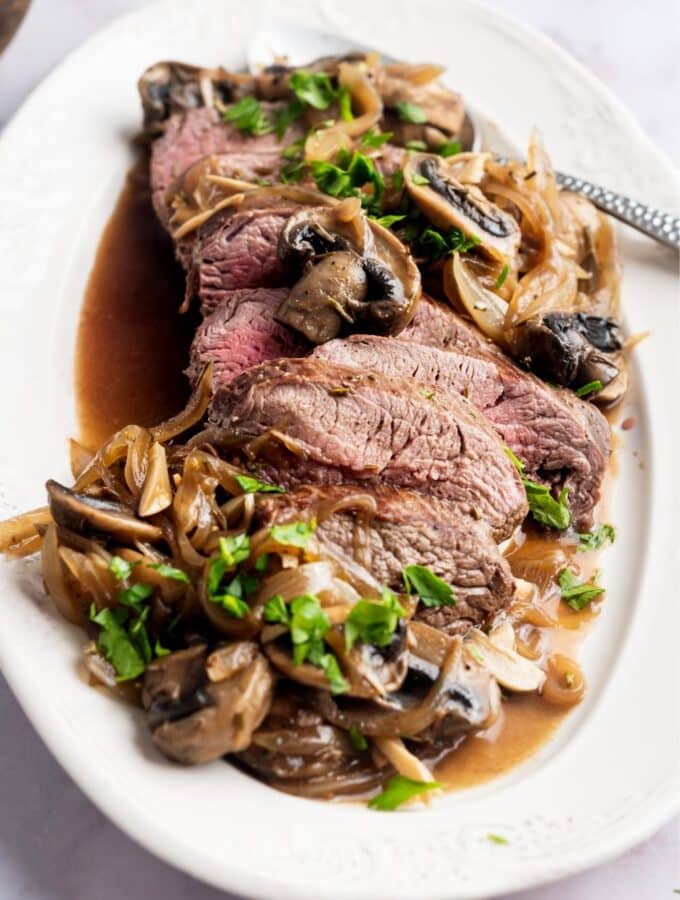 Bottom round roast that is slice with mushrooms and onions surrounding it on a plate.