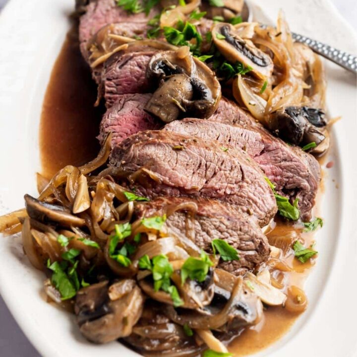 Bottom round roast that is slice with mushrooms and onions surrounding it on a plate.