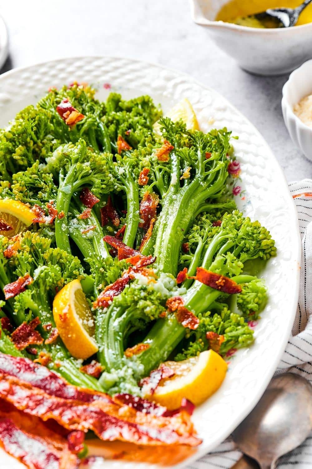 Slices of bacon, lemon wedges, and broccolini on a white plate.