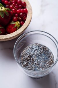 Chia seed putting a glass bowl. Behind it is part of a bowl of berries.