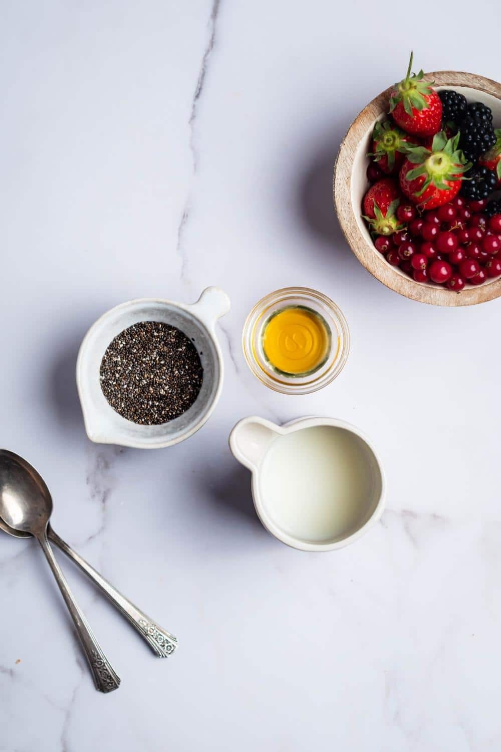 Chia seeds in a bowl, milk in a bowl, honey in a bowl, and fresh berries in a bowl.