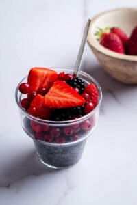 Fresh strawberries, blackberries, and cherries on top of Chia seeds in a glass bowl.