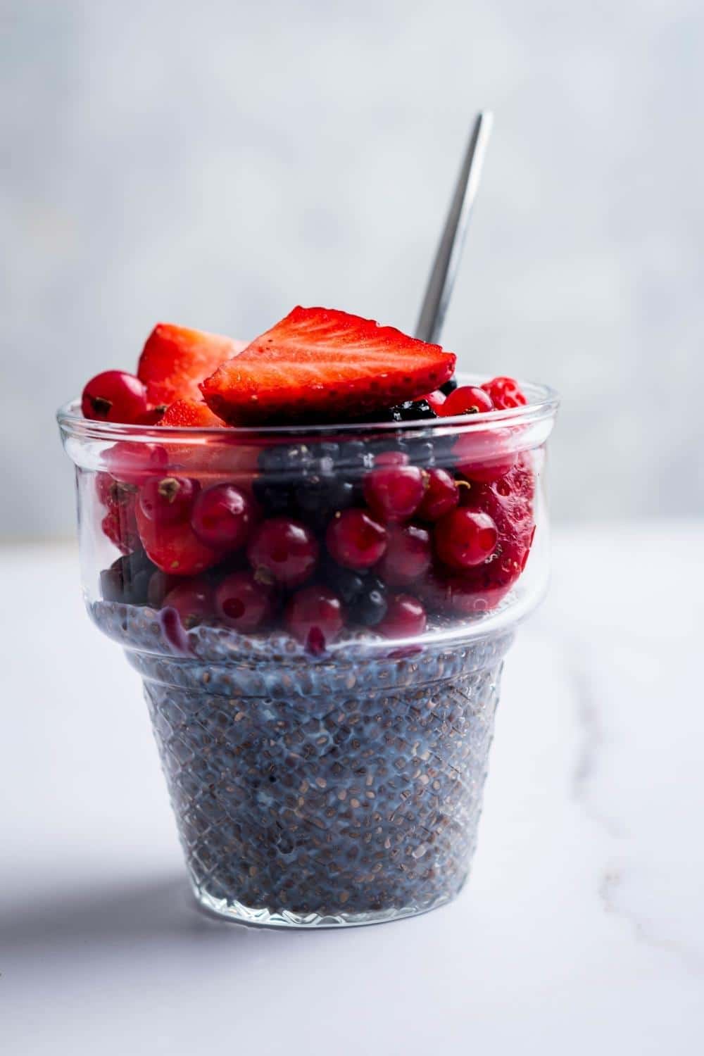 Strawberries, blackberries, and cherries on top of Chia seeds in a glass container.