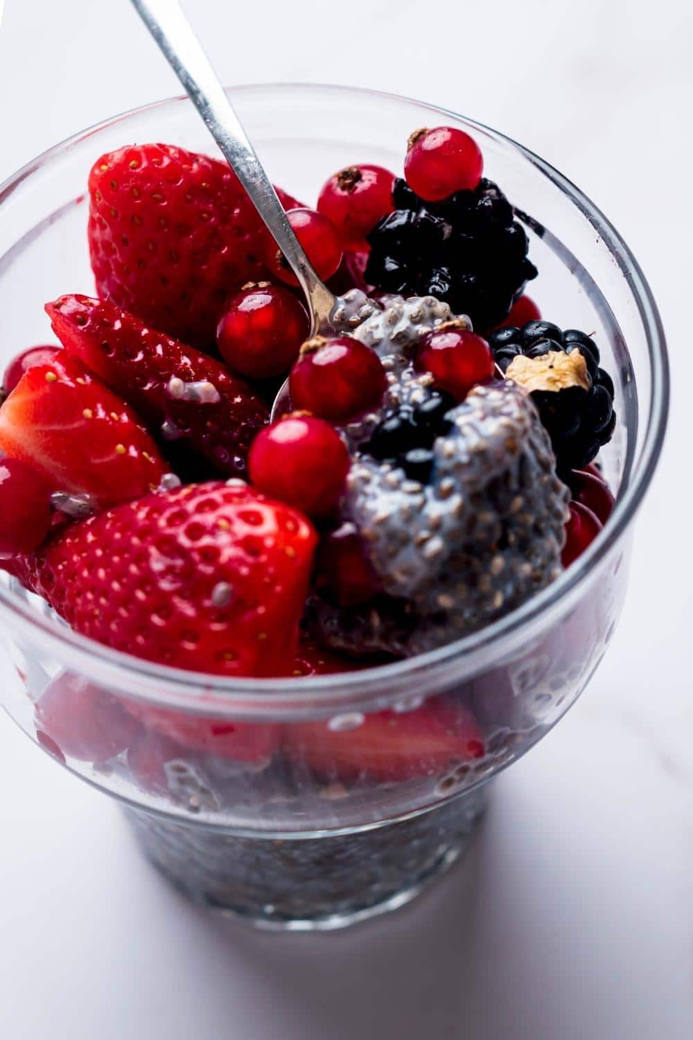 A spoon with some Chia seed putting in it with blackberries, strawberries, and cherries on top.