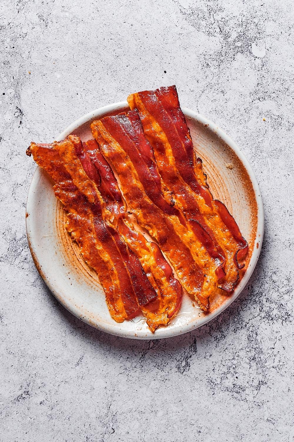 Five slices of crispy bacon on a plate on a grey counter.