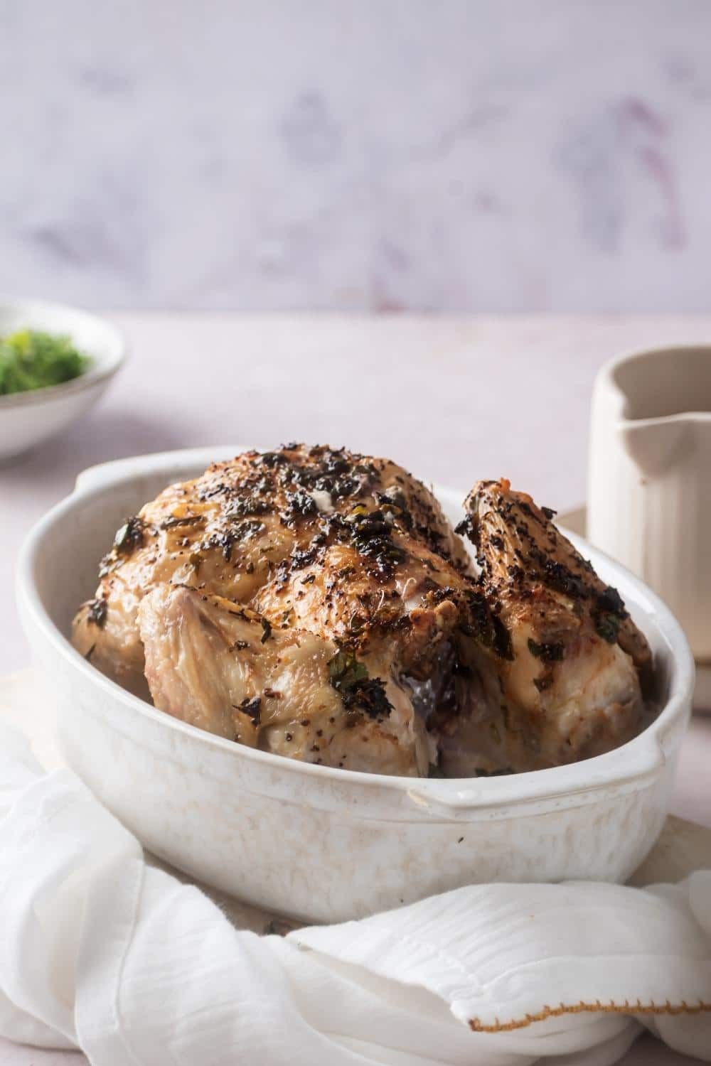 A cornish hen in a white casserole dish.