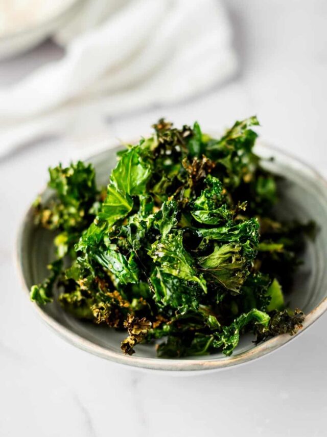 Kale chips in a white bowl on a white counter.