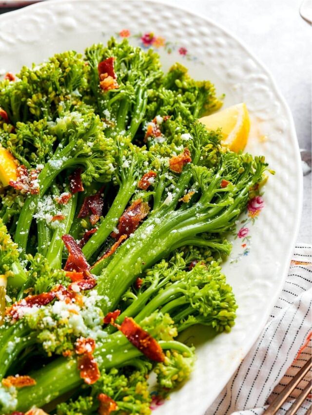 A couple of broccolini stalks with pieces of bacon on part of a white plate.