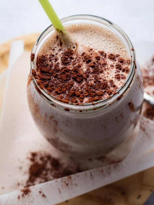 A mass gainer protein shake in a glass with a straightener and cocoa powder on top.