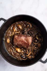 Bottom round roast with mushrooms and onions in a Dutch oven.