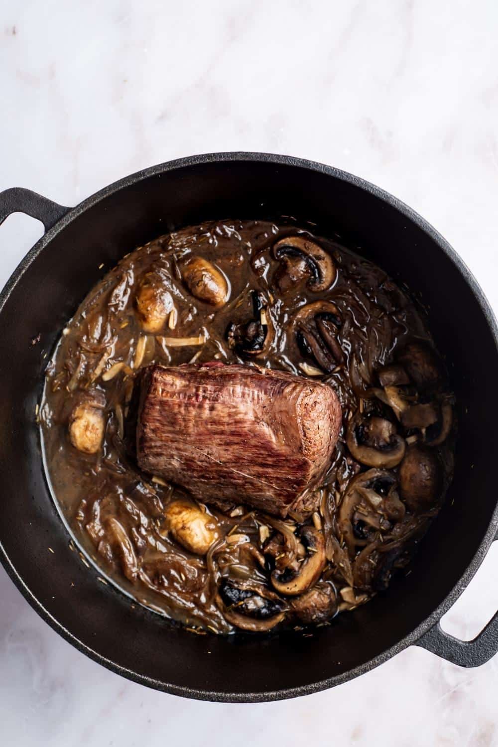 Bottom round roast with mushrooms and onions in a Dutch oven.