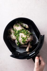 A hand holding an air fryer basket with a cornish hen in it.