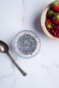 Chia seeds and milk in a glass bowl. Behind it is part of a bowl filled with berries.