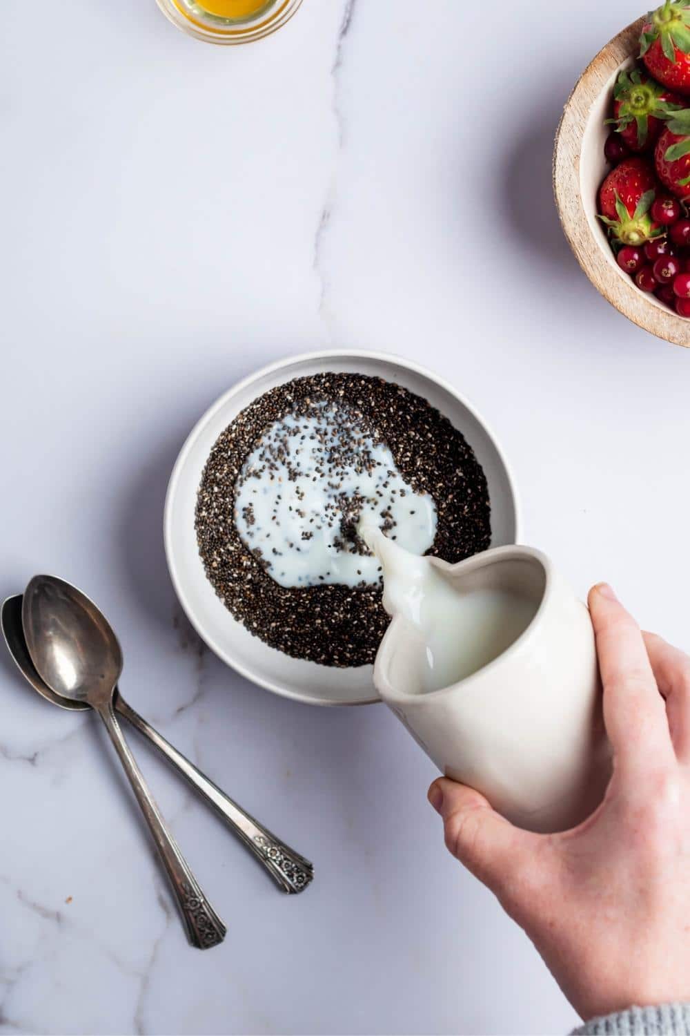 A hand pouring milk into a bowl that is filled with chia seeds.