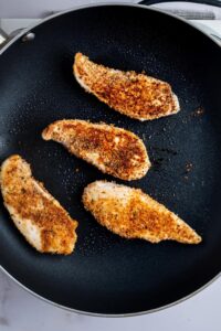 Four chicken breasts in a skillet.