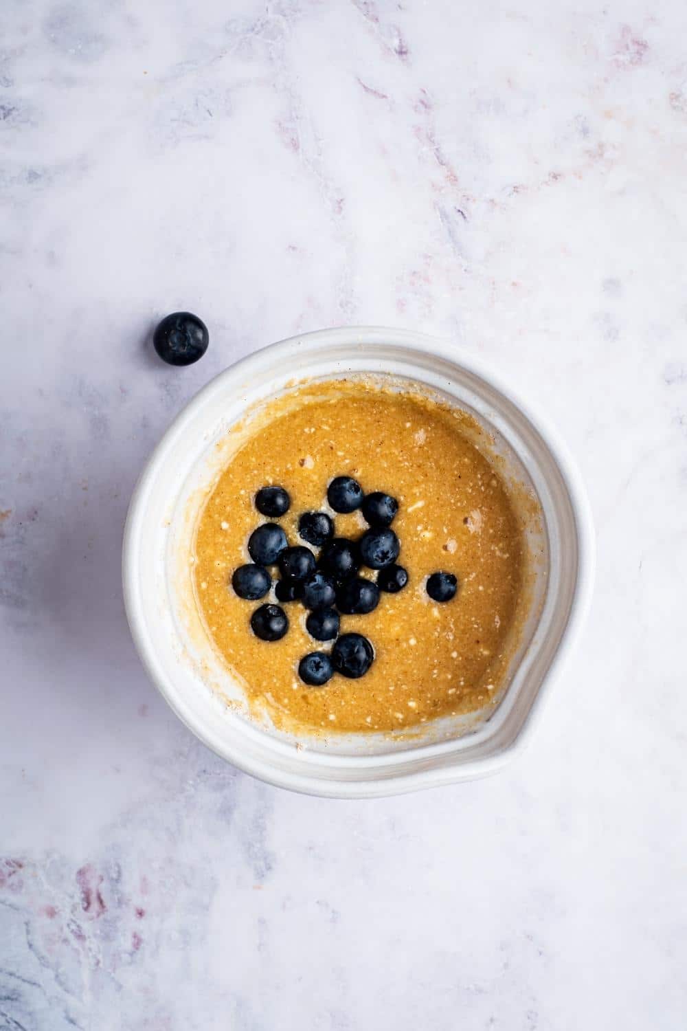 Blueberries on top of batter and white ball on a gray counter.