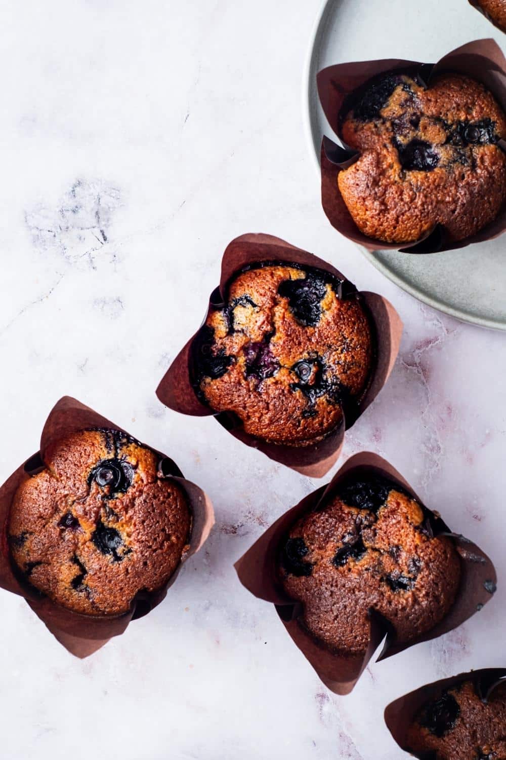 Four blueberry muffins in muffin tins on the counter.