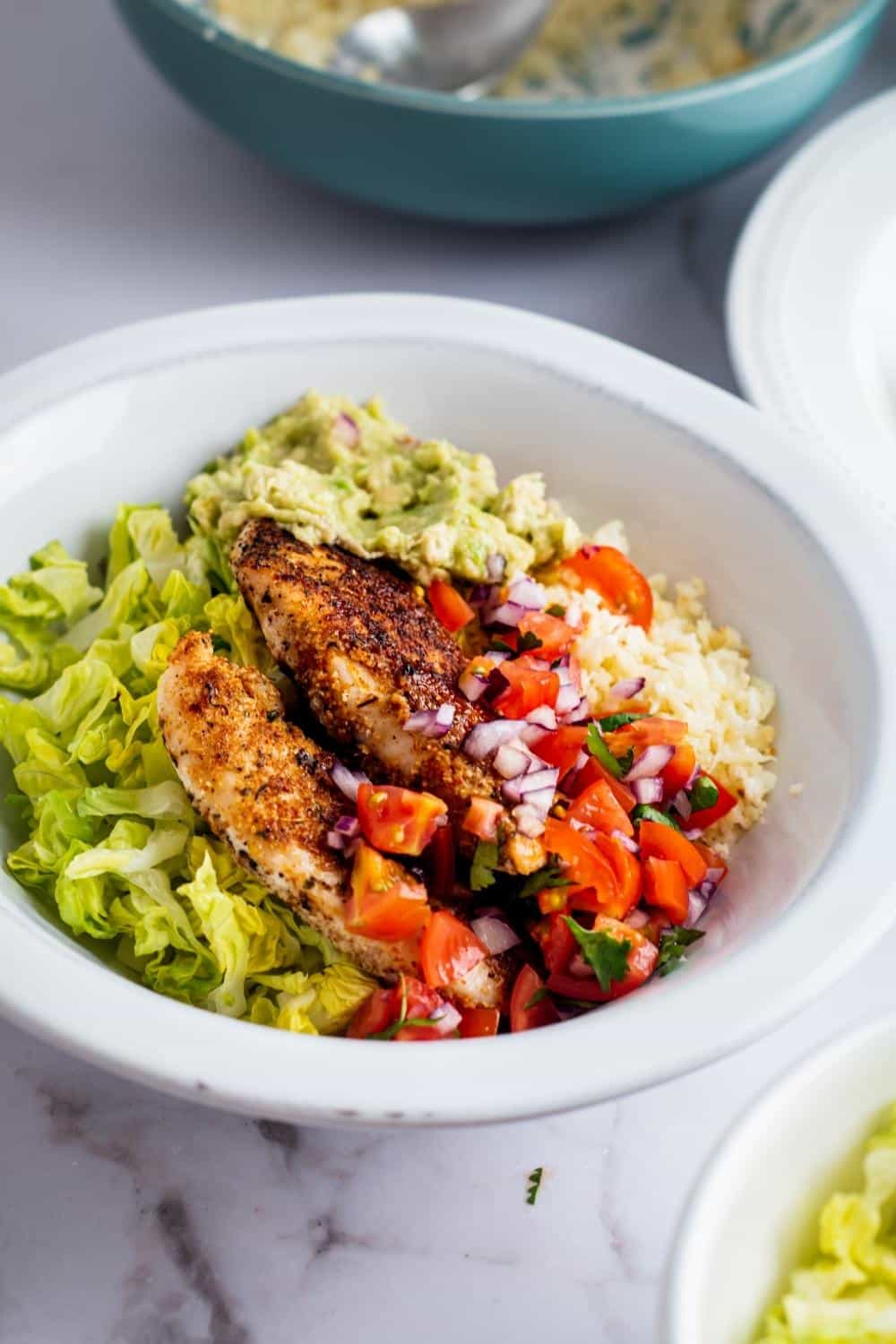 Chicken breasts, pico, lettuce, guac, and cauliflower rice in a bowl.