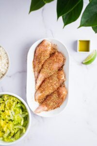 Seasoned chicken on a plate and part of a bowl of lettuce.