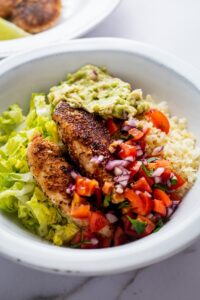 Chicken breasts, pico, lettuce, and guac with cauliflower rice in a bowl.