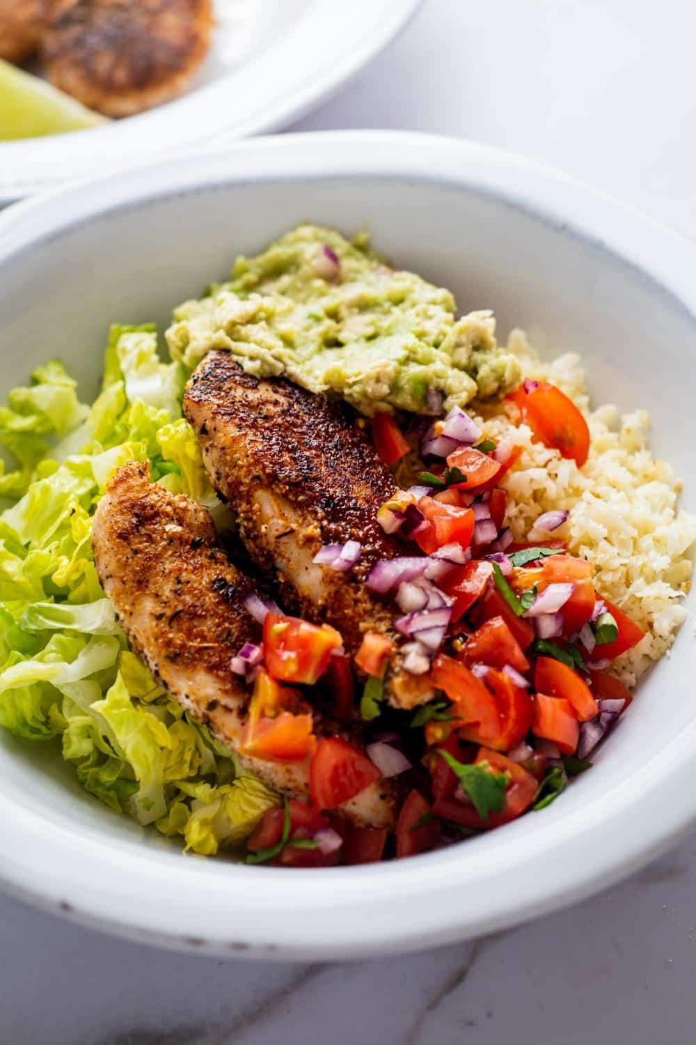 Chicken breasts, pico, lettuce, and guac with cauliflower rice in a bowl.