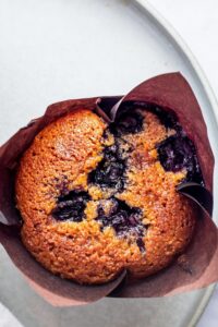 A blueberry muffin and a muffin tin on top of part of a plate.