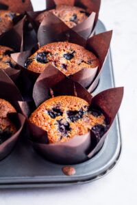 A row of three keto blueberry muffins in muffin paper in a muffin tray.