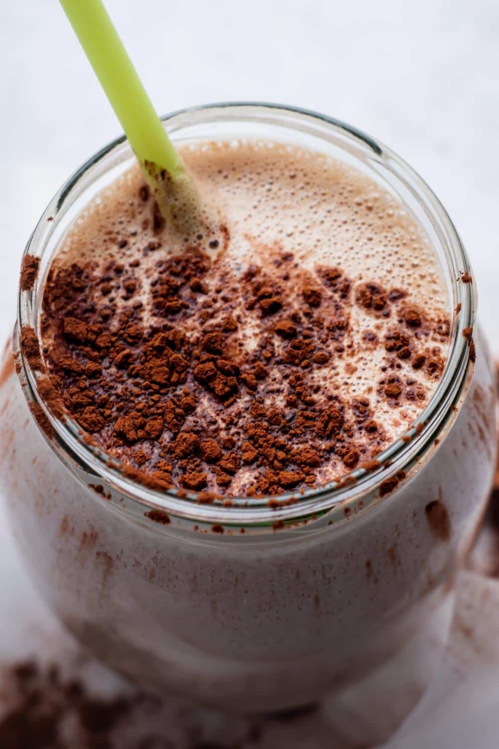 Mass gainer smoothie in a glass with cocoa powder on top.