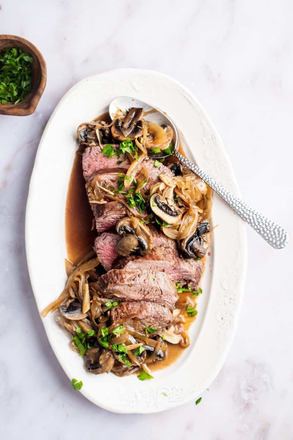 Slices of a bottom round roast with mushrooms and onions on a white plate.