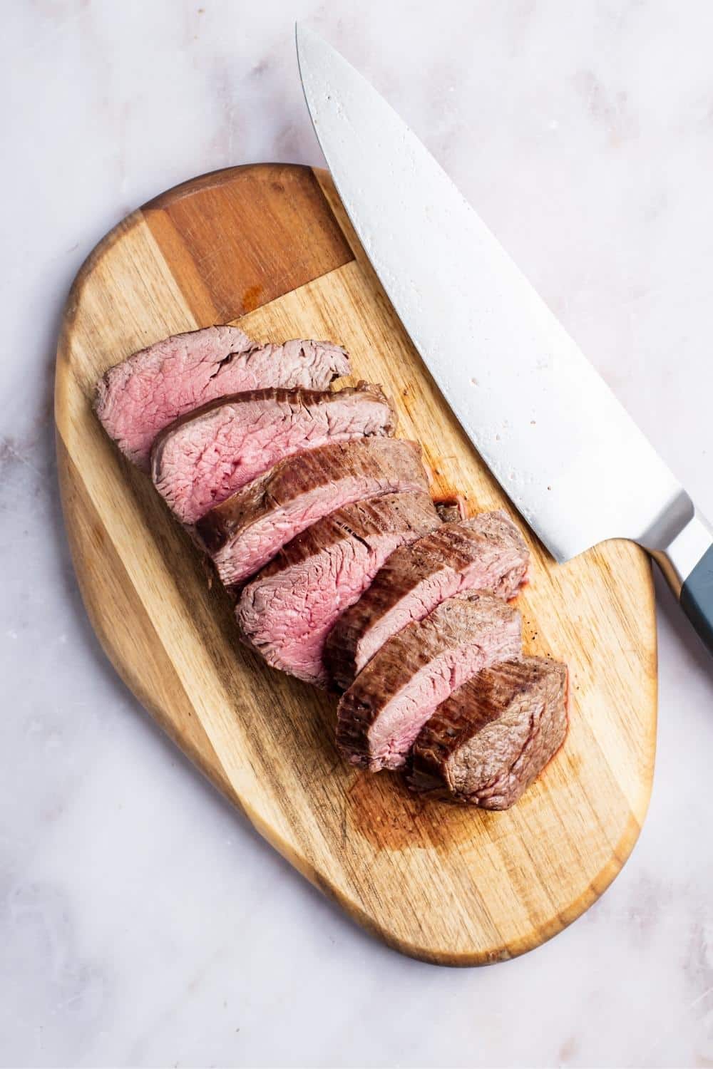 A bottom round roast sliced into eight slices on top of a wooden cutting board with a knife next to it.