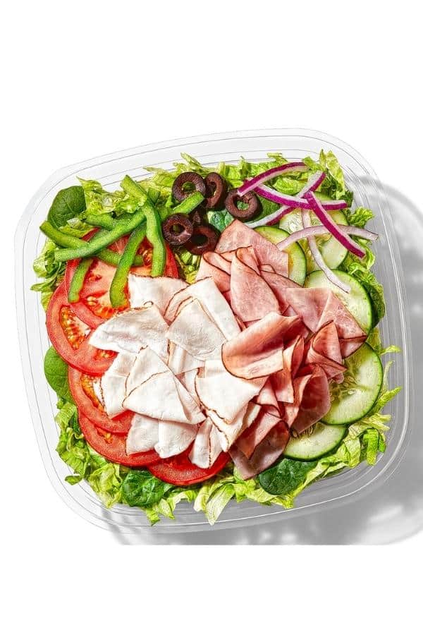 Turkey and ham along with cucumbers, tomatoes, green peppers, red onion, and black olives on top of lettuce in a container.