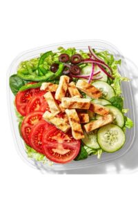 Grilled chicken strips, tomato, cucumber, black olives, red and green onion on top of lettuce in a container.