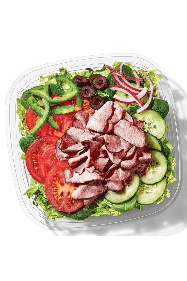 Roast beef, tomatoes, green pepper, olives, red onion on top of lettuce in a container.