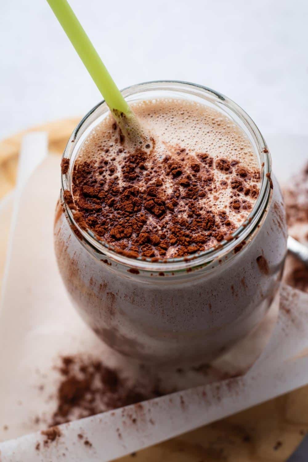 A mass gainer protein shake in a glass with a straightener and cocoa powder on top.