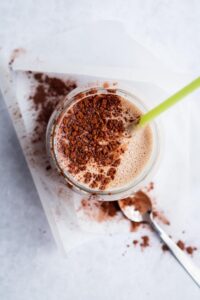 Cocoa powder on top of a mass gainer shake in a glass.