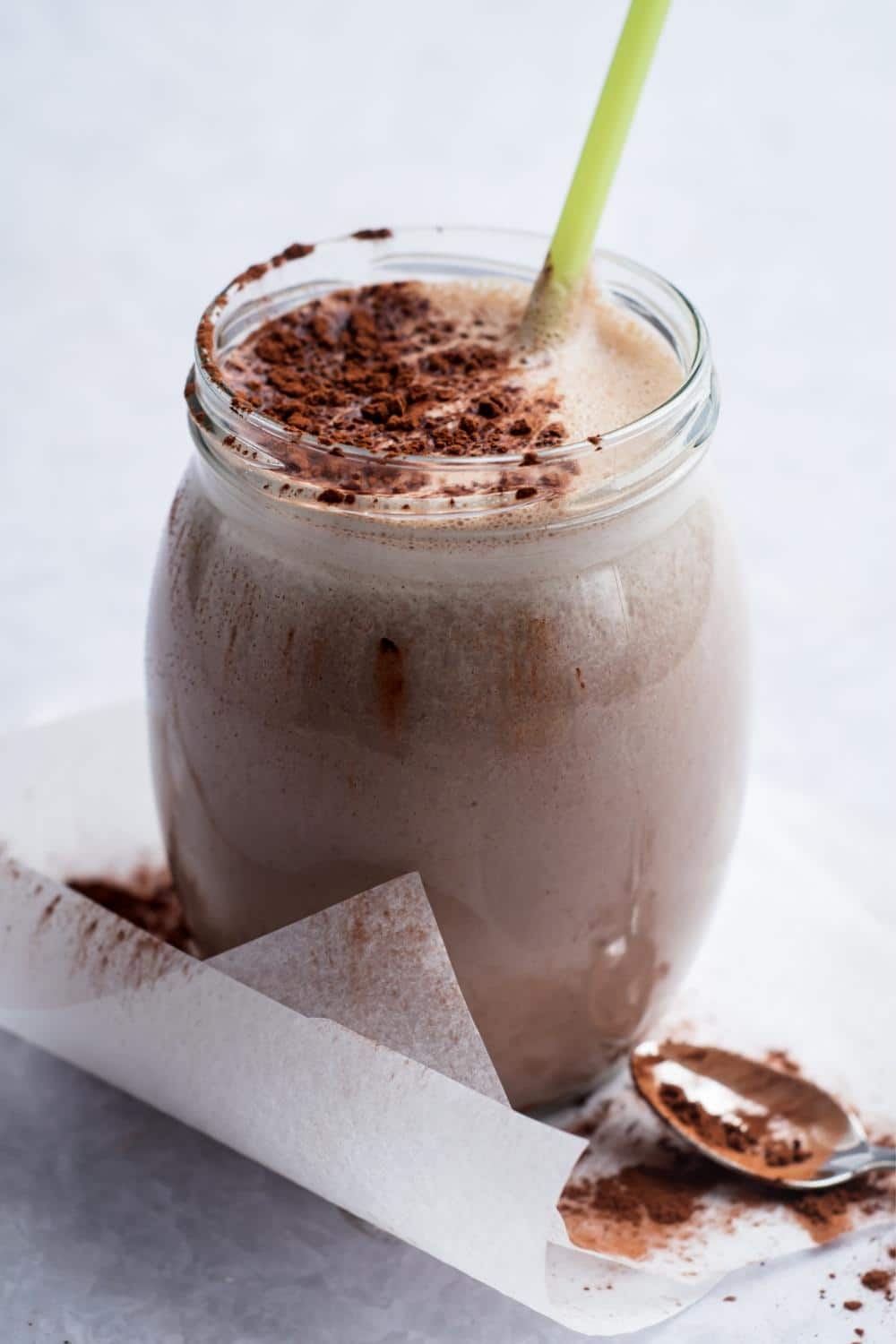 A mass gainer shake in a glass. It has cocoa powder on top and a green straw in it.